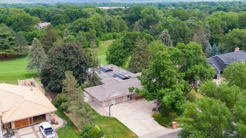 Aerial view of a suburban neighborhood with green trees, houses, and a driveway in a lush, landscaped area.