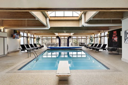 Indoor swimming pool with diving board, lounge chairs, and large windows letting in natural light.