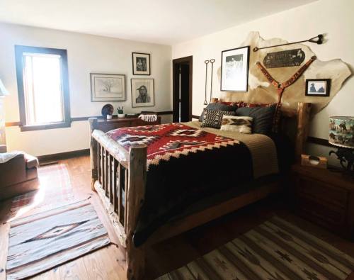 Cozy bedroom featuring a wooden bed, patterned blankets, artwork, and rustic decor in warm tones.