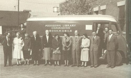 A group of people stands in front of a vintage bookmobile, labeled "Mississippi Library Commission."