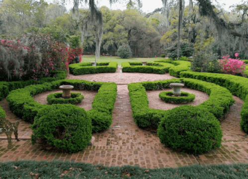 A beautifully manicured garden with symmetrical hedges, stone paths, and vibrant flowering plants.