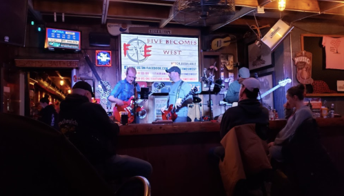 A live band performs on stage in a bar, with audience members seated and enjoying the music.