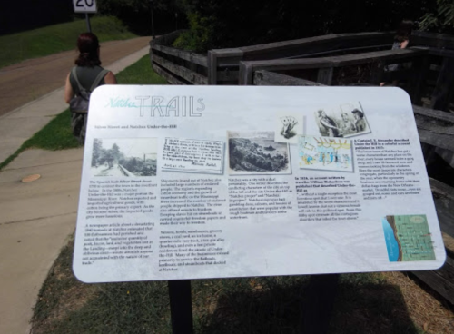 A person walks past an informational sign about trails, featuring historical images and text.