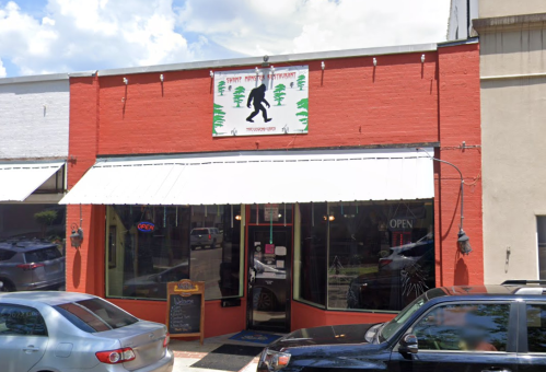 Exterior of a restaurant with a red facade, featuring a Bigfoot sign and an "Open" banner, surrounded by parked cars.