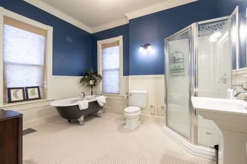 A stylish bathroom featuring a clawfoot tub, glass shower, and blue walls with natural light from two windows.