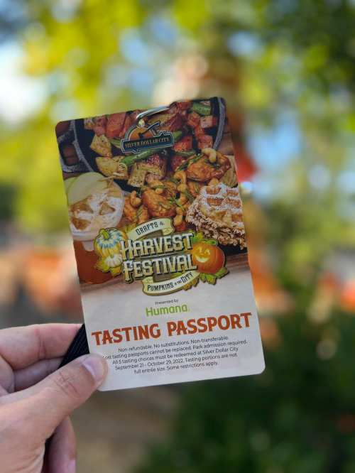 A hand holding a "Tasting Passport" for the Harvest Festival, featuring food images and festive graphics.