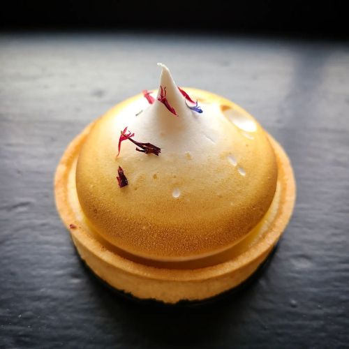 A round dessert with a golden top, adorned with a peak of meringue and sprinkled with colorful flower petals.