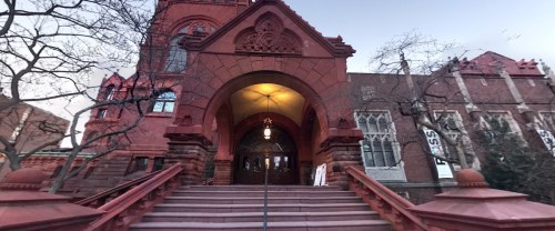 Historic red brick building with an arched entrance and steps, surrounded by bare trees and a clear sky.