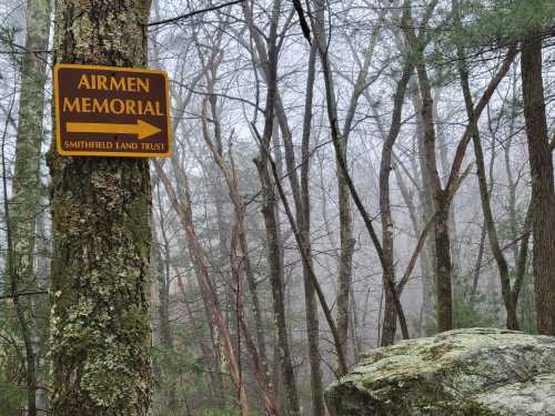 A sign for the Airmen Memorial points left, surrounded by foggy trees and rocky terrain.