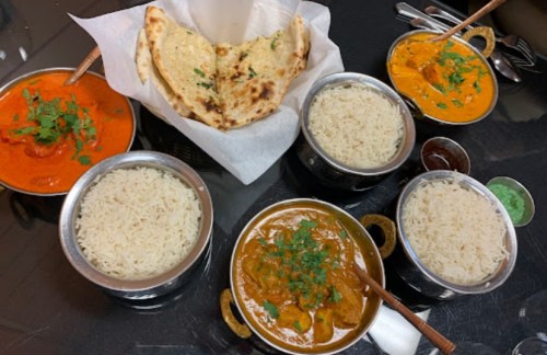 A spread of Indian dishes featuring rice, curry, and naan, garnished with cilantro on a black table.