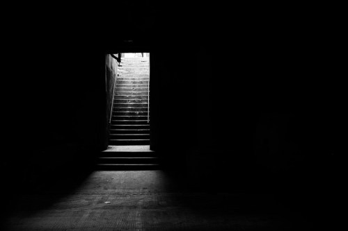 A dark corridor with a staircase leading to a bright light at the top, creating a stark contrast.