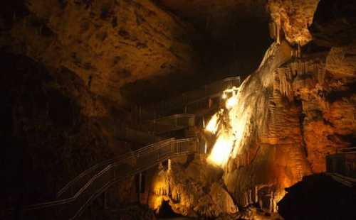 Dimly lit cave interior with rock formations and metal stairs leading deeper into the cavern.