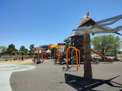 A colorful playground with slides, swings, and climbing structures under a clear blue sky. Trees in the background.