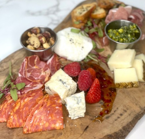 A wooden platter featuring assorted meats, cheeses, fruits, nuts, and spreads, beautifully arranged for a charcuterie board.