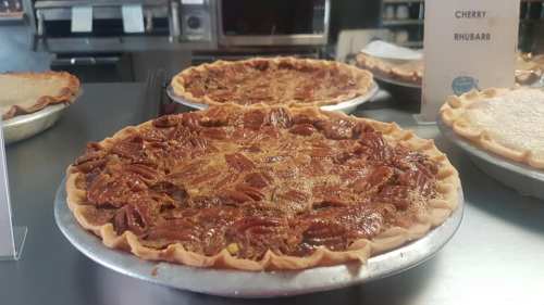 Two freshly baked pecan pies on display, with a sign for cherry rhubarb pie in the background.