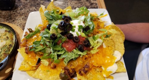 A plate of nachos topped with cheese, lettuce, black olives, salsa, and sour cream.