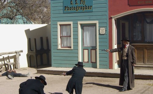 A Wild West scene with cowboys in a gunfight outside a photographer's shop. Dusty street and historic buildings visible.