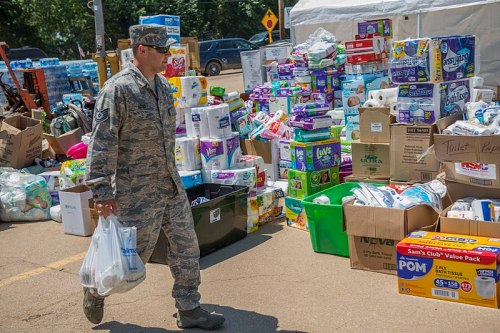A military personnel walks past a large collection of donated supplies, including toiletries and paper products.