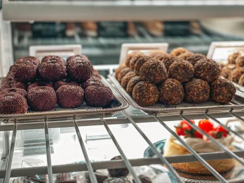 Two trays of assorted sweet treats: chocolate-covered balls and nutty energy bites, displayed in a glass case.