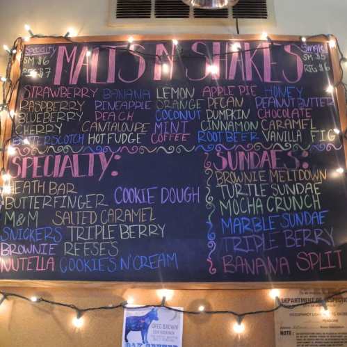 Chalkboard menu listing milkshakes and sundaes with flavors like strawberry, cookie dough, and banana split.