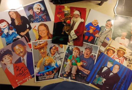 A collection of signed photos featuring clowns, puppets, and performers, arranged on a table.