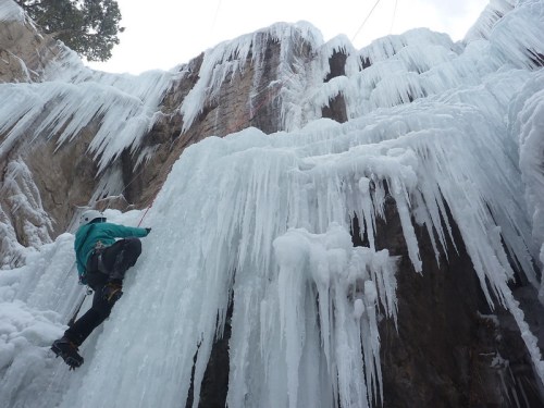 A climber ascends a frozen waterfall, surrounded by icicles and icy rock formations.