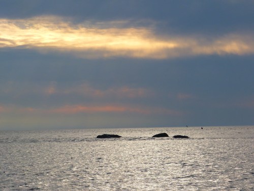 A serene seascape at dusk, featuring three rocks in calm waters under a cloudy sky with hints of sunset colors.