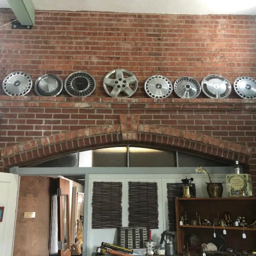 A brick wall displays a row of vintage hubcaps above an arched doorway, with various decorative items below.