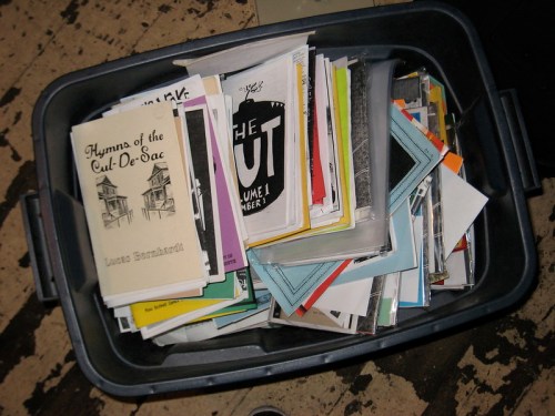 A plastic bin filled with various colorful papers, booklets, and pamphlets stacked haphazardly inside.