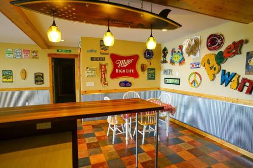 A cozy room with a wooden table, white chairs, and colorful wall signs, including a surfboard hanging from the ceiling.