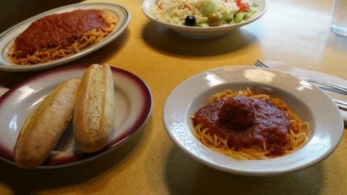 A plate of spaghetti with meatballs and marinara sauce, accompanied by two breadsticks and a side salad.