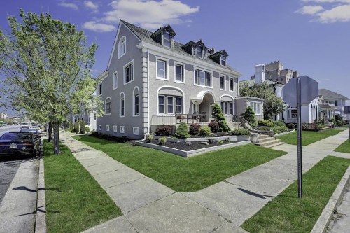 A large, elegant gray house with a manicured lawn and trees, located on a quiet street.