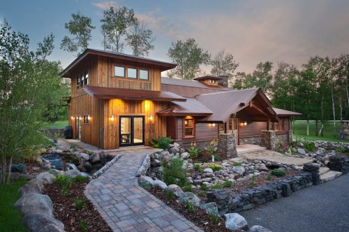 A modern wooden house with large windows, surrounded by greenery and a stone pathway leading to the entrance.