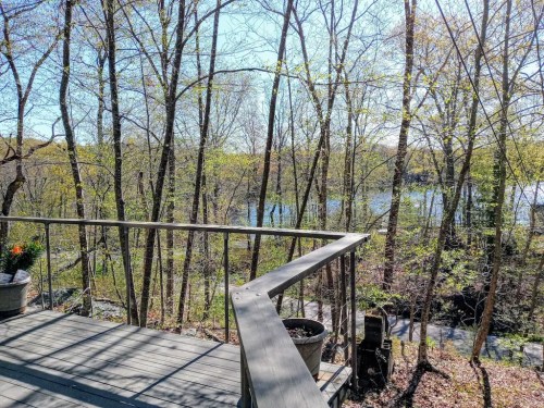 A wooden deck overlooks a serene river surrounded by trees and greenery on a sunny day.