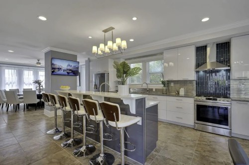 Modern kitchen with a large island, bar stools, stainless steel appliances, and a dining area in the background.