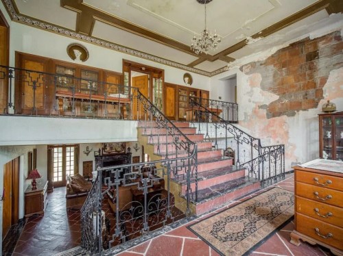 A spacious foyer with a staircase, wooden cabinets, and a mix of elegant and worn decor.