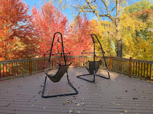 Two hanging chairs on a wooden deck surrounded by vibrant autumn foliage in red, orange, and yellow.