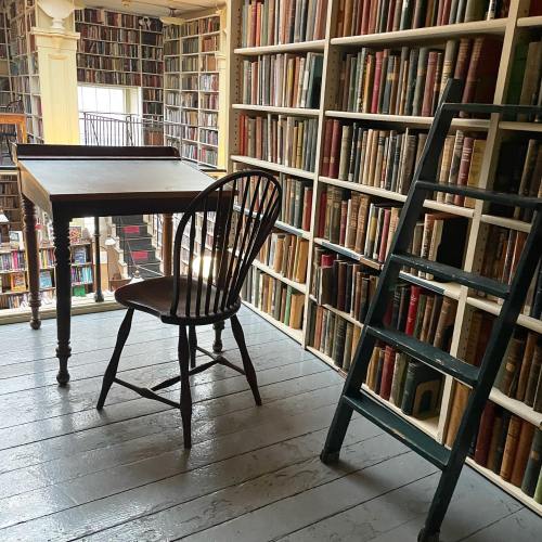 A cozy library corner with a wooden desk, chair, and a ladder beside shelves filled with books.