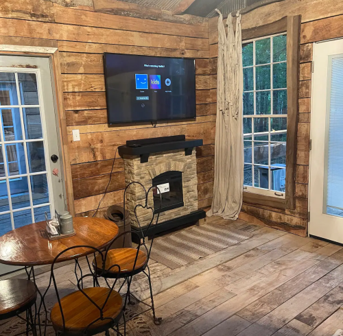 Cozy interior with wooden walls, a small dining table, a TV on the wall, and a stove near a large window.