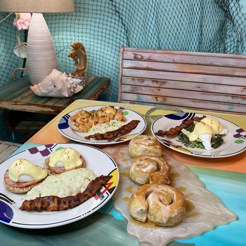 A colorful table setting with plates of eggs Benedict, bacon, seafood, and cinnamon rolls, surrounded by beach-themed decor.