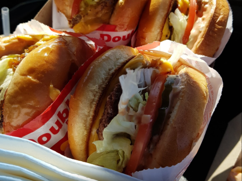 A close-up of several burgers with lettuce, tomato, and cheese, served in a tray.