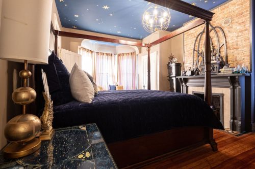Cozy bedroom with a four-poster bed, starry ceiling, and warm lighting, featuring a decorative fireplace and stylish decor.