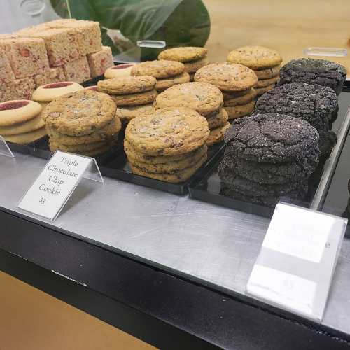A display case with various cookies, including triple chocolate chip and chocolate cookies, priced at $3 each.