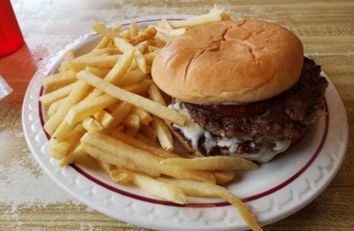 A plate with a hamburger topped with sauce and a side of golden French fries.