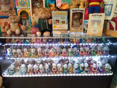 A display case filled with colorful toys, including teddy bears and small figurines, illuminated by LED lights.