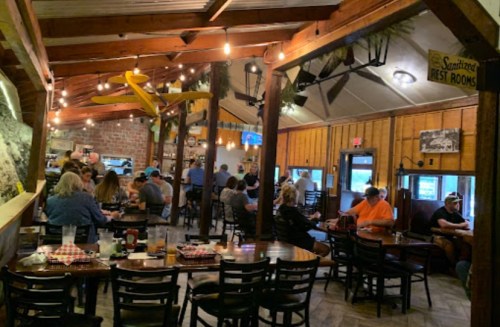 A bustling restaurant interior with wooden beams, patrons dining, and warm lighting creating a cozy atmosphere.