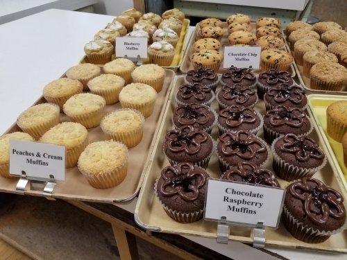 A display of assorted muffins: blueberry, peaches & cream, chocolate chip, and chocolate raspberry, all labeled.