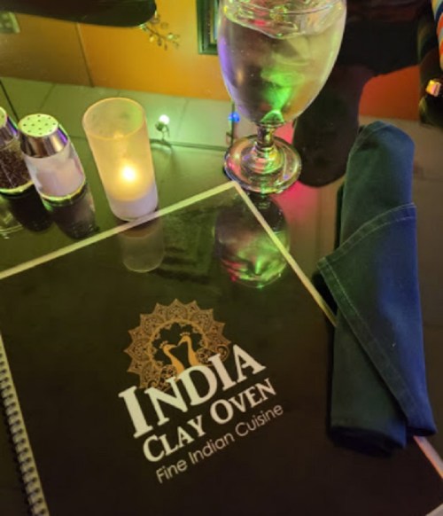A table setting featuring a menu for "India Clay Oven," a glass of water, and a candle.