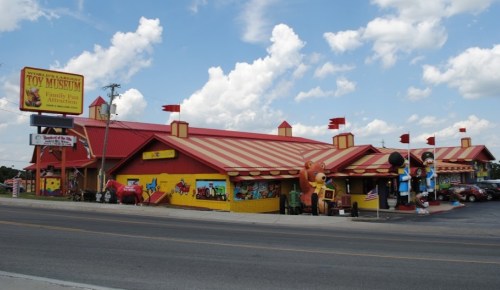 Colorful toy museum with a striped roof, large toy figures outside, and a sign advertising family fun activities.