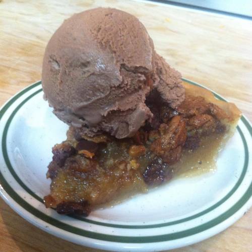 A slice of pecan pie topped with a scoop of chocolate ice cream on a white plate.